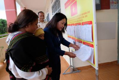 Chị Dà Ju K’Kim (thôn Long Lanh) được cán bộ xã Lạc Dương hỗ trợ kiểm tra thông tin của vợ chồng chị trong danh sách cử tri niêm yết tại UBND xã Lạc Dương. Ảnh: Nguyễn Dũng – TTXVN
